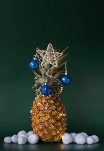 istock Christmas decor concept with pineapple, blue balls, white stars and artificial snowballs on green background. Copy space 1785900121