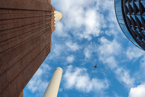 London, England. November 7th 2023. Looking up between Battersea power station and a modern building a plane can be seen flying over the capital.