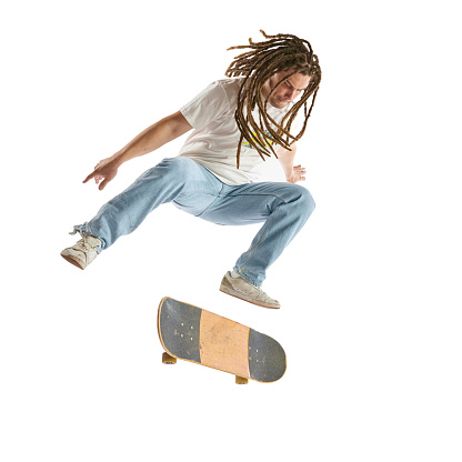 Full length portrait of man skateboarder performing freestyle tricks in motion isolated white studio background. Concept of youth culture, active lifestyle, style and fashion, creativity, art. Ad