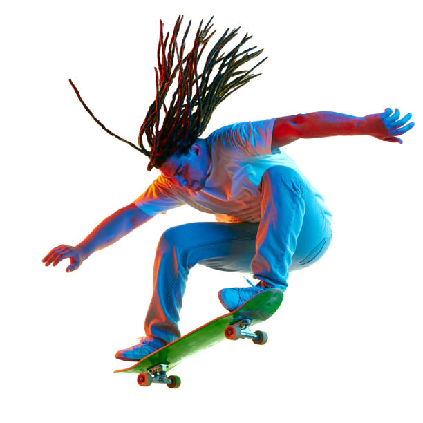 Action shot of a young Gen Z skateboarder with long dreadlocks tied in a ponytail, performing a jump over a set of stairs in a public park. He is wearing jeans and a white sleeveless T-shirt, captured mid-air with his skateboard. A dynamic moment of youth, energy, and modern skateboarding culture
