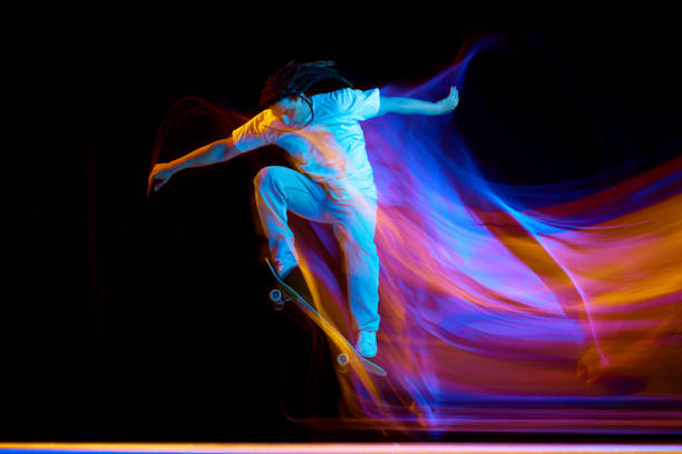 istock Man skateboarder performing freestyle tricks in motion isolated black studio background in mixed neon flashes of light. Concept of youth culture. 1785916959