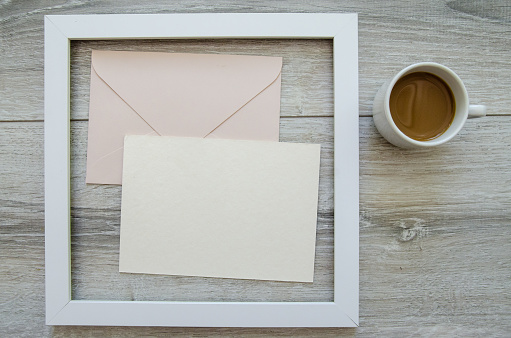 Minimal composition flatlay with a cup of coffee in white wooden frame and mockup and copyspace pastel pink envelopes and blank postcard