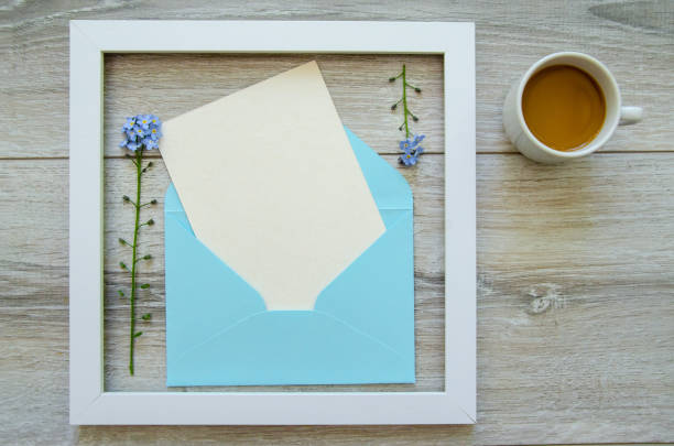 istock Flatlay gray natural wooden background with square white wooden frame and blue envelope white postcard copyspace, small blue flowers on a branch 1785920268