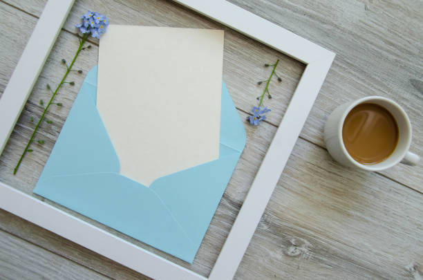 istock Flatlay gray natural wooden background with square white wooden frame and blue envelope white postcard copyspace, small yellow flowers and green leaves on a branch 1785921419