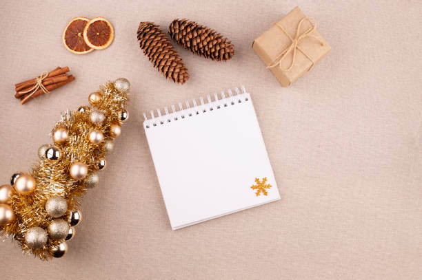 istock Christmas holiday background with diary and golden colored tree, cinnamon sticks and gift wrapped in kraft paper, dried oranges on linen fabric background, flat lay, copy space. 1785936166