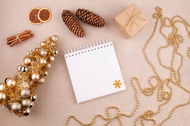istock Christmas holiday background with diary and golden colored tree, cinnamon sticks and gift wrapped in kraft paper, dried oranges on linen fabric background, flat lay, copy space. 1785936216