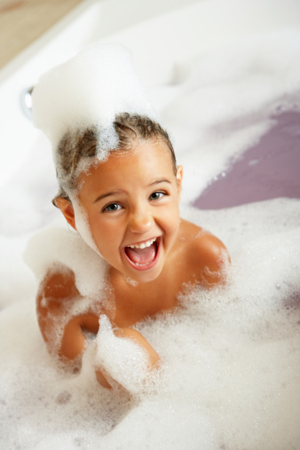 Girl Playing In Bath Sitting Down Smiling At Camera