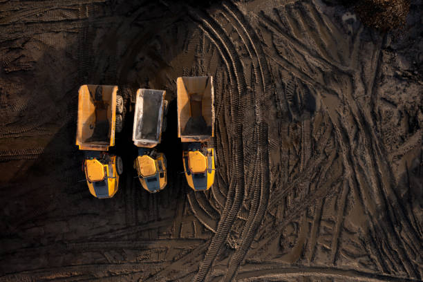 Aerial view above earth mover trucks on a muddy construction site Aerial view directly above industrial dumper truck or earth mover vehicle with muddy soil and tyre tracks in the construction industry on a brownfield site with copy space construction vehicle stock pictures, royalty-free photos & images