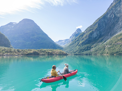 Happy couple with a red inflatable canoe on peaceful environment in Norway. Blue lake and green mountains