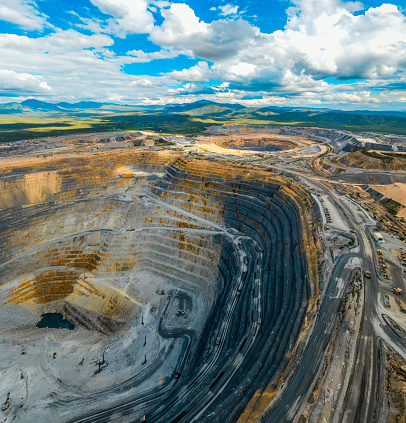Panoramic view of two open pit mines, with blue sky and mountains in the background.