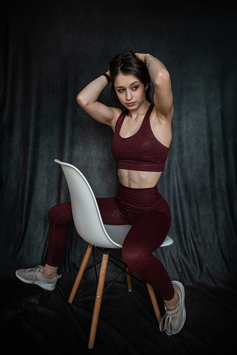 young slim woman in red sport cloth bra posign near chair isolated on black. lifestyle
