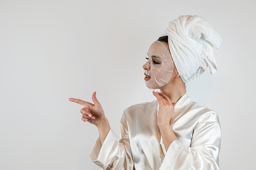 Pretty lady applying moisturizing and tightening mask isolated on white. Spa treatments and skin care