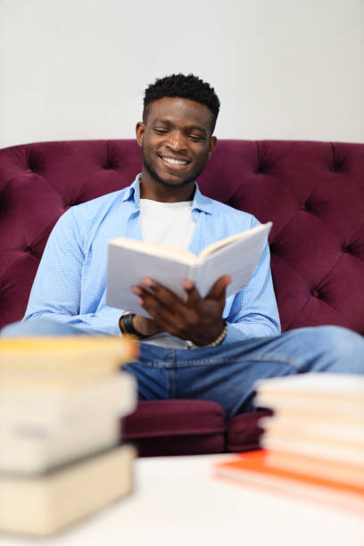 istock adult student smiling, studying on a sofa in a home library, surrounded by books. 1785968216