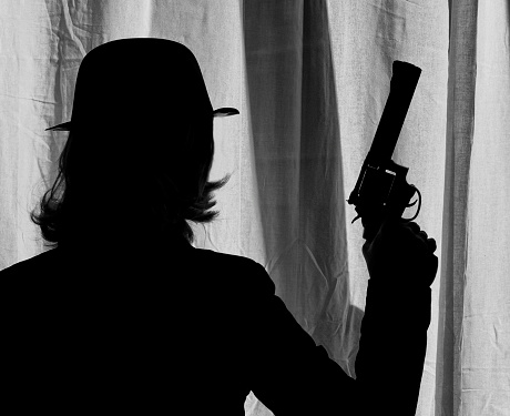 Silhouette of a woman with gun hiding behind a window.