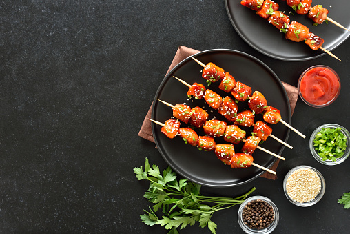 Teriyaki chicken skewers on plate over black background with copy space. Top view, flat lay