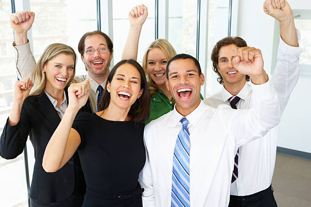 Portrait Of Business Team In Office Celebrating Portrait Of Business Team In Office Celebrating Looking At Camera Cheering cheering group of people success looking at camera stock pictures, royalty-free photos & images