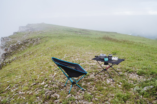 Hiking kitchen camping equipment stands on the mountain against the background of nature, a folding camping chair, camping furniture. High quality photo
