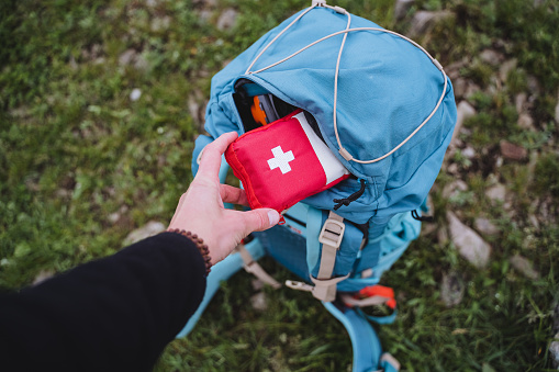 A first aid kit is in a backpack, a hand holds a bag of medicines, an open pocket of a bag, road medicine assistance, camping equipment. High quality photo