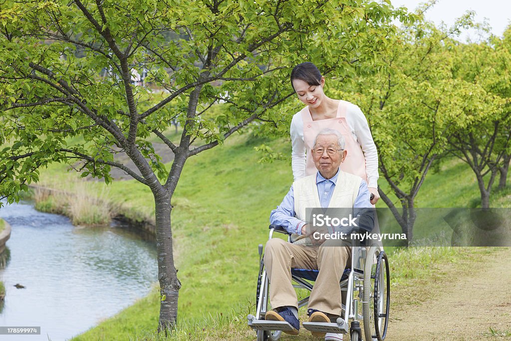 Sênior homem sentado em uma cadeira de rodas com cuidadora - Foto de stock de Adulto royalty-free