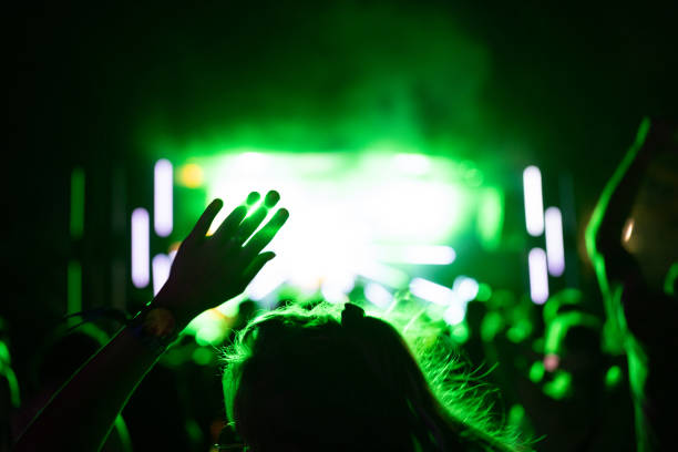 tłum ludzi uczestniczących w występie muzycznym z rękami w górze. jasnozielone promienie światła dochodzące ze sceny - arms raised green jumping hand raised zdjęcia i obrazy z banku zdjęć