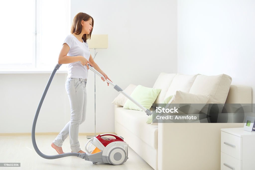 Attractive girl vacuuming a white couch Attractive girl with vacuum cleaner on light background Vacuum Cleaner Stock Photo