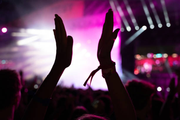 istock Crowd of people attending a musical performance and clapping. Bright pink light rays coming from the stage 1786023588