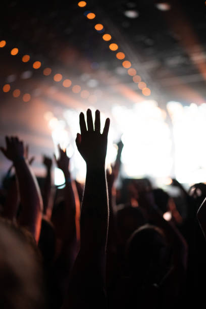 istock Crowd of people attending a musical performance. Putting hands up. Bright light effects coming from the stage 1786023709