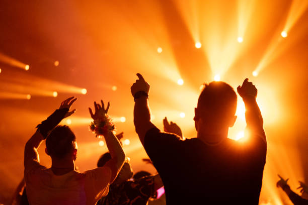 istock Crowd of people attending a musical performance. Audience dancing illuminated by orange reflector lights 1786024130