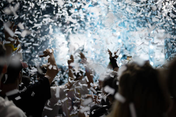 istock Crowd of people attending a musical performance. Putting hands up. White confetti falling down on audience 1786024150