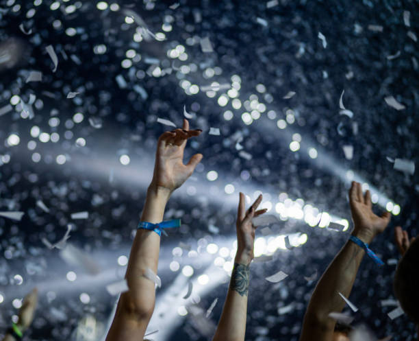 istock Crowd of people attending a musical performance. Putting hands up. White confetti falling on excited audience 1786024690
