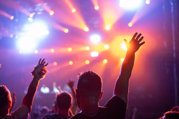 istock Crowd of people attending a musical performance. Audience dancing illuminated by red lights coming from stage 1786024695