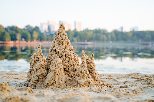 Wet sand lake shore, city recreation park, sand castle, sand drops, pond in the background, landscape in the morning. High quality photo