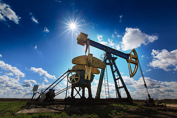 An oil and gas well against a sunny sky Operating oil and gas well profiled on bright sky with clouds in active European oilfield shale stock pictures, royalty-free photos & images