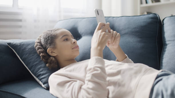 istock Cute black girl using social network app in smartphone, lying on sofa at home 1786052216