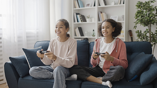 Happy teen sisters sincerely smiling, playing video game together, relationship