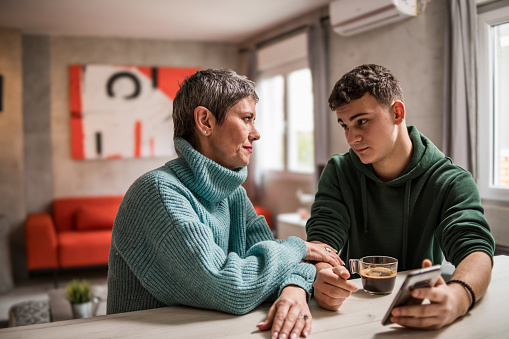 A mother and son are sitting at home and talking, helping her son solve his teenage problems