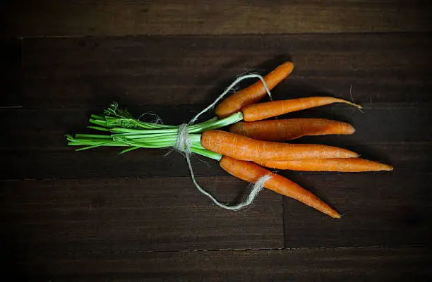 Photo of Carrots with greens, tied on brown wood