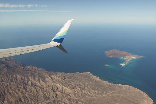 Loreto, Mexico – May 13, 2019: An aerial view of an island featuring a plane wing in the sky against a backdrop of lush green vegetation and shimmering blue oceans