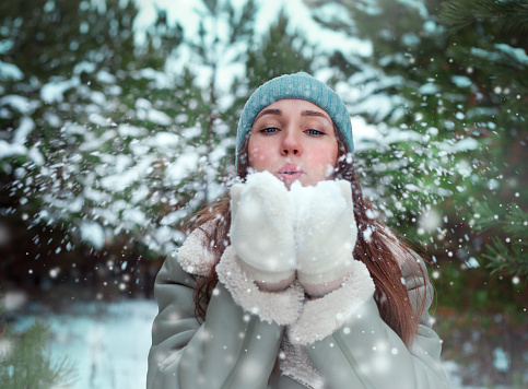 Close-up portrait of a young woman blowing snowflakes in a winter forest