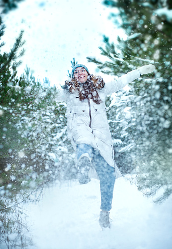 Laughing girl playfully kicks snow in the forest in winter