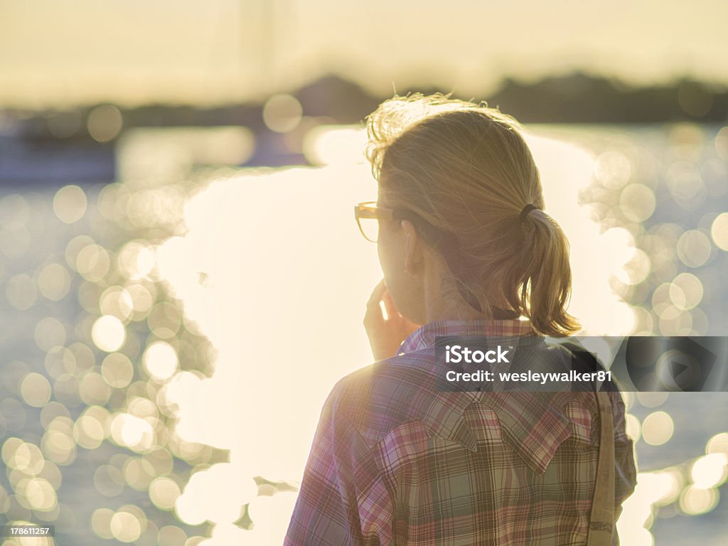 Thoughtful woman looking at lake with bokeh reflections Woman standing at the edge of a bay staring out at the water while thinking or relaxing. Adult Stock Photo