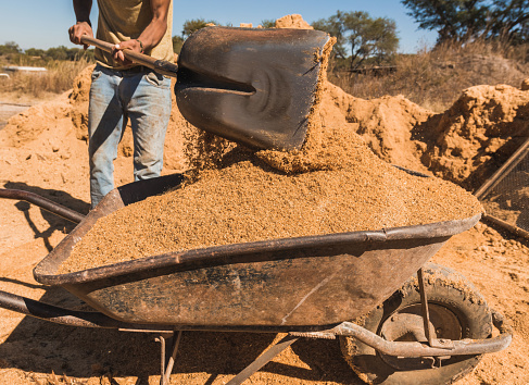 Worker of a brick factory strains sand with a shovel in a wheelbarrow, for the elaboration of bricks.