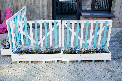 Decorative fence near the entrance to the house, a barrier of boards, wooden pots with flowers, the design of the street space in front of the cafe on the sidewalk. High quality photo
