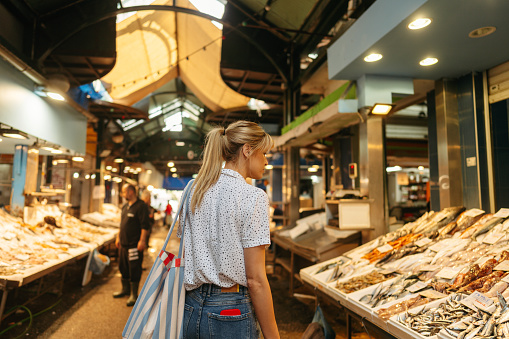 Photo of a young woman buying fresh fish and seafood on the local fish market; experiencing local places, activities and food, and meeting local people while traveling.
