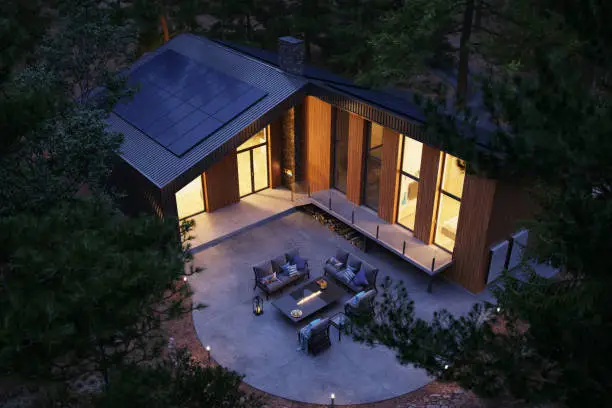 Modern forest house equipped with solar panels and an energy storage wall battery during dusk.