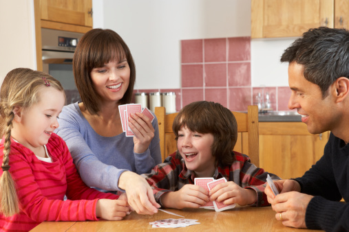 Family Playing Cards In Kitchen Sitting Around Table Laughing