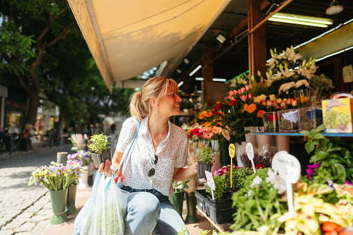 Photo of a young woman buying flowers and herbs in a local flower shop; experiencing local places, activities and food, and meeting local people while traveling.