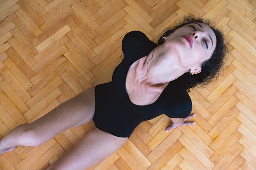 A ballet dancer posing while lying on a wooden floor.