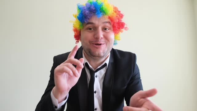 A dancing young man in a colorful wig moves his hands rhythmically against a studio background