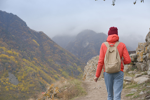 A free woman traveler walks along paths in the mountains on a foggy autumn day. Adventure travel and success concept.